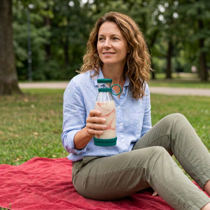 Blender smoothie turquoise et une femme assise au parc sur une serviette rouge